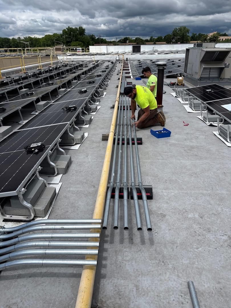 J.E.N.S Electric crew bending and laying galvanized conduit on a commercial roof beside solar panels
