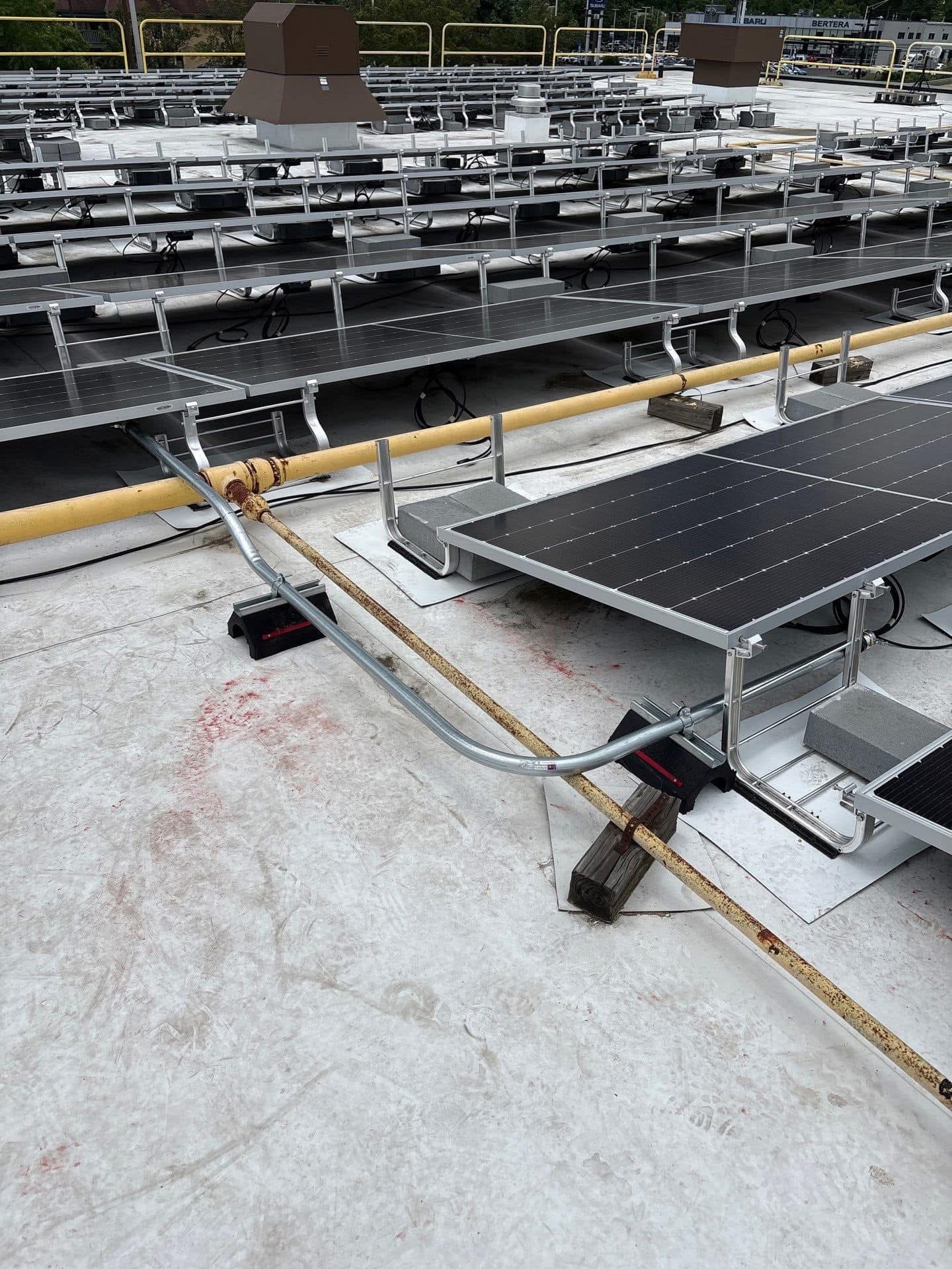 Galvanized conduit routed around a gas line between rows of rooftop solar panels